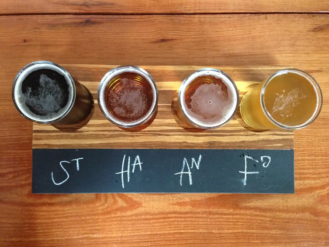 Four beers in small glasses on a wooden board, seen from above