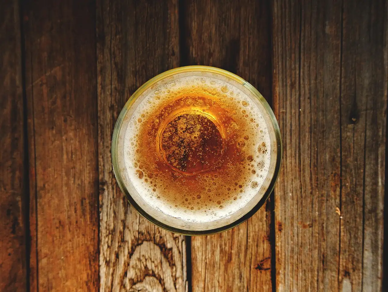 A glass of beer seen from above on an old wooden table