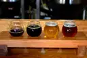 Four small glasses of different beers on a wooden tasting paddle