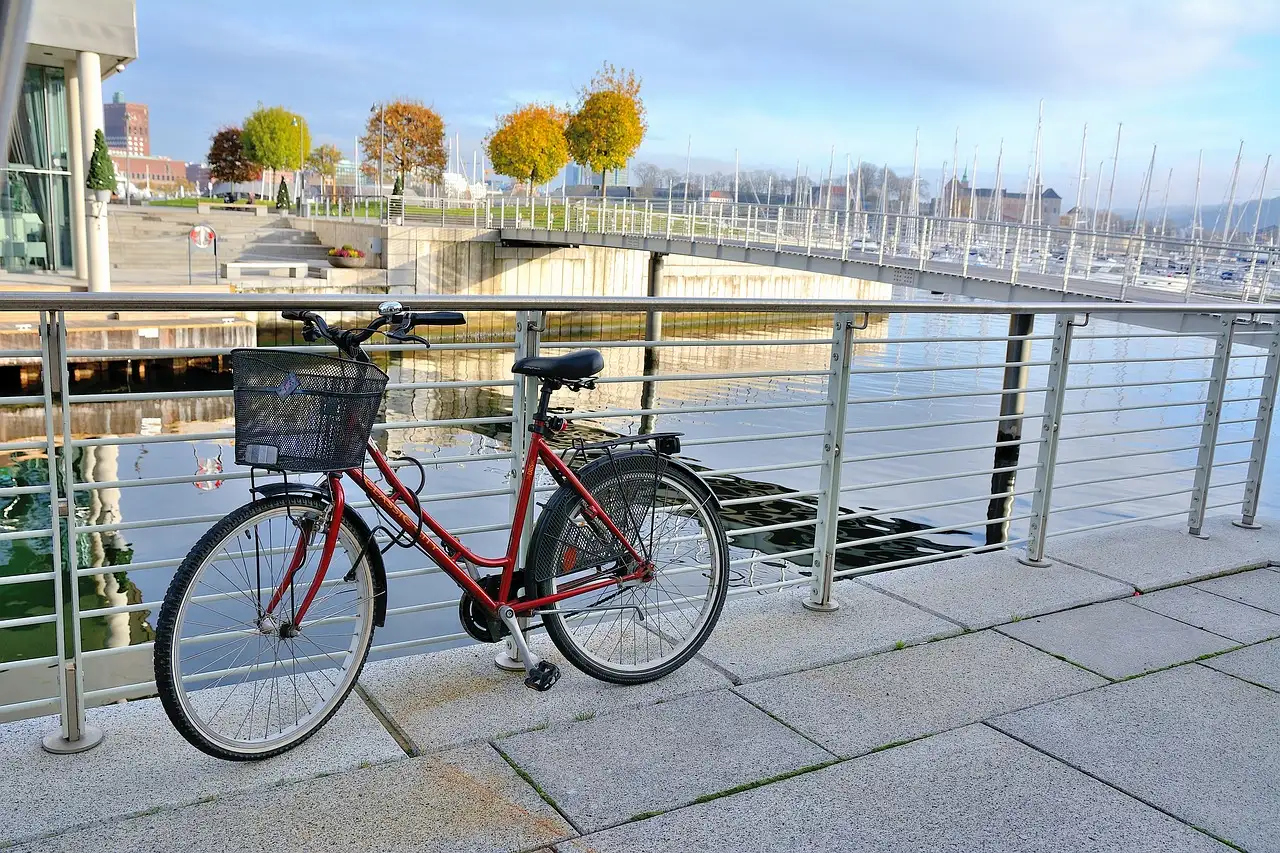 Red bicycle with a basket leaning on a railing by a waterfront path and marina