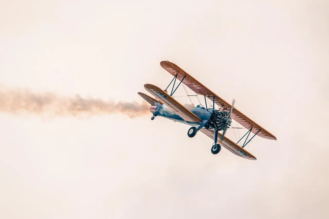 A vintage biplane flying with a trail of white smoke behind it