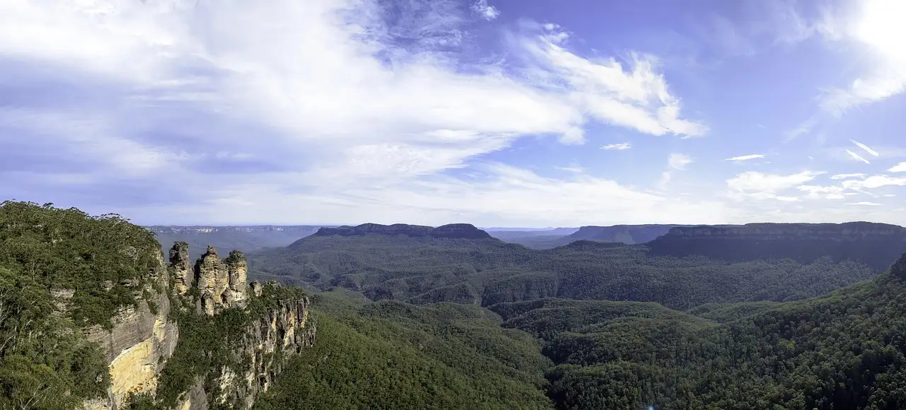 A wide view over the forested Jamison Valley in the Blue Mountains, with the Three Sisters on the left