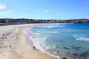 Long curve of Bondi Beach with pale sand, turquoise surf and houses along the shore on a sunny day