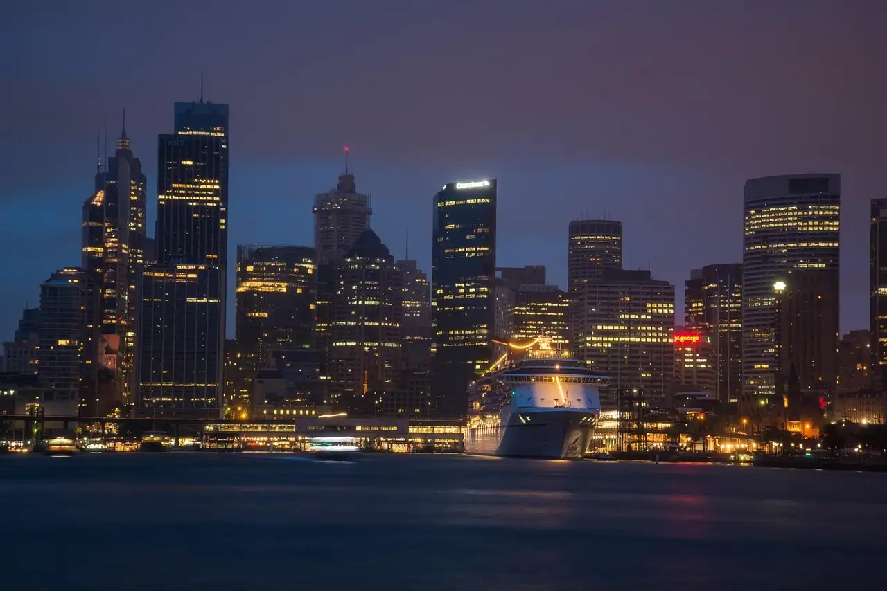 Circular Quay at dusk, with a cruise ship at the terminal and the lit city towers behind