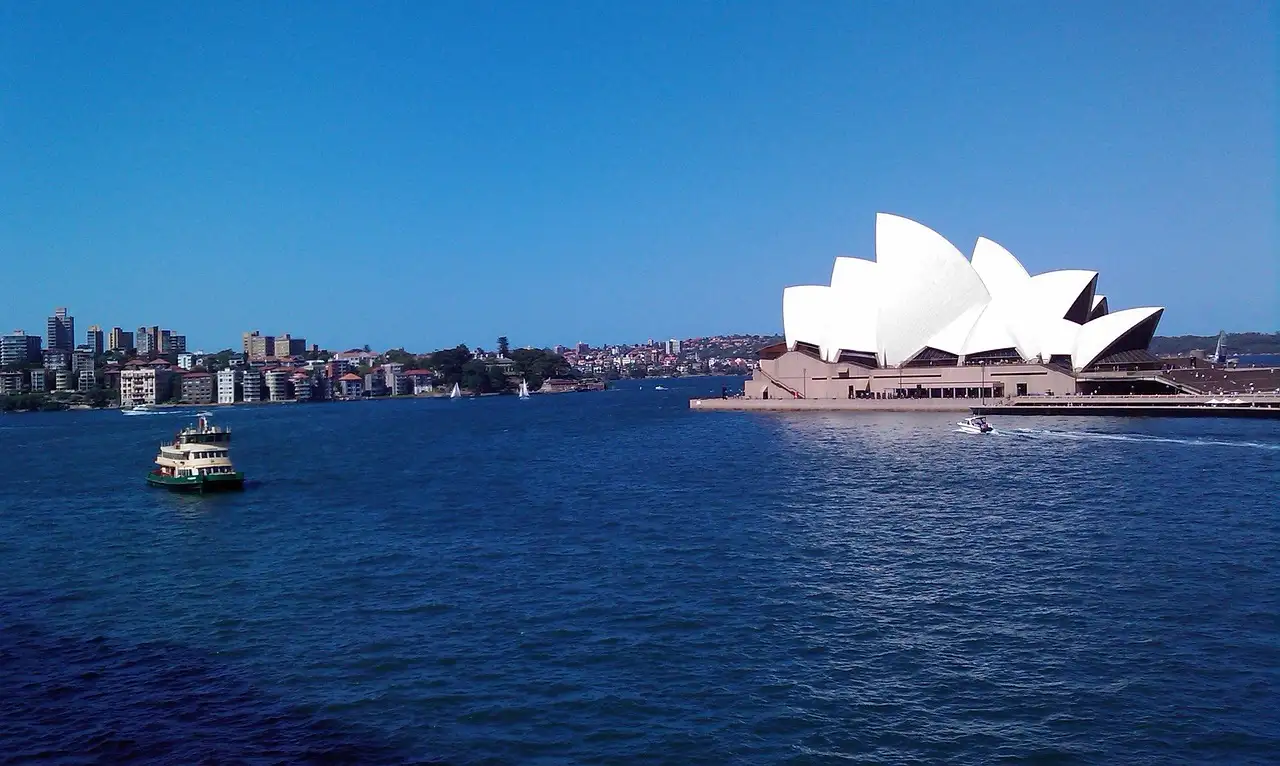 A small cruise boat on Sydney Harbour passing the Sydney Opera House