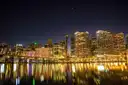 The lit-up city skyline at night, reflected in the water
