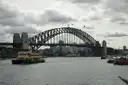 The Sydney Harbour Bridge on a cloudy day, with a ferry below