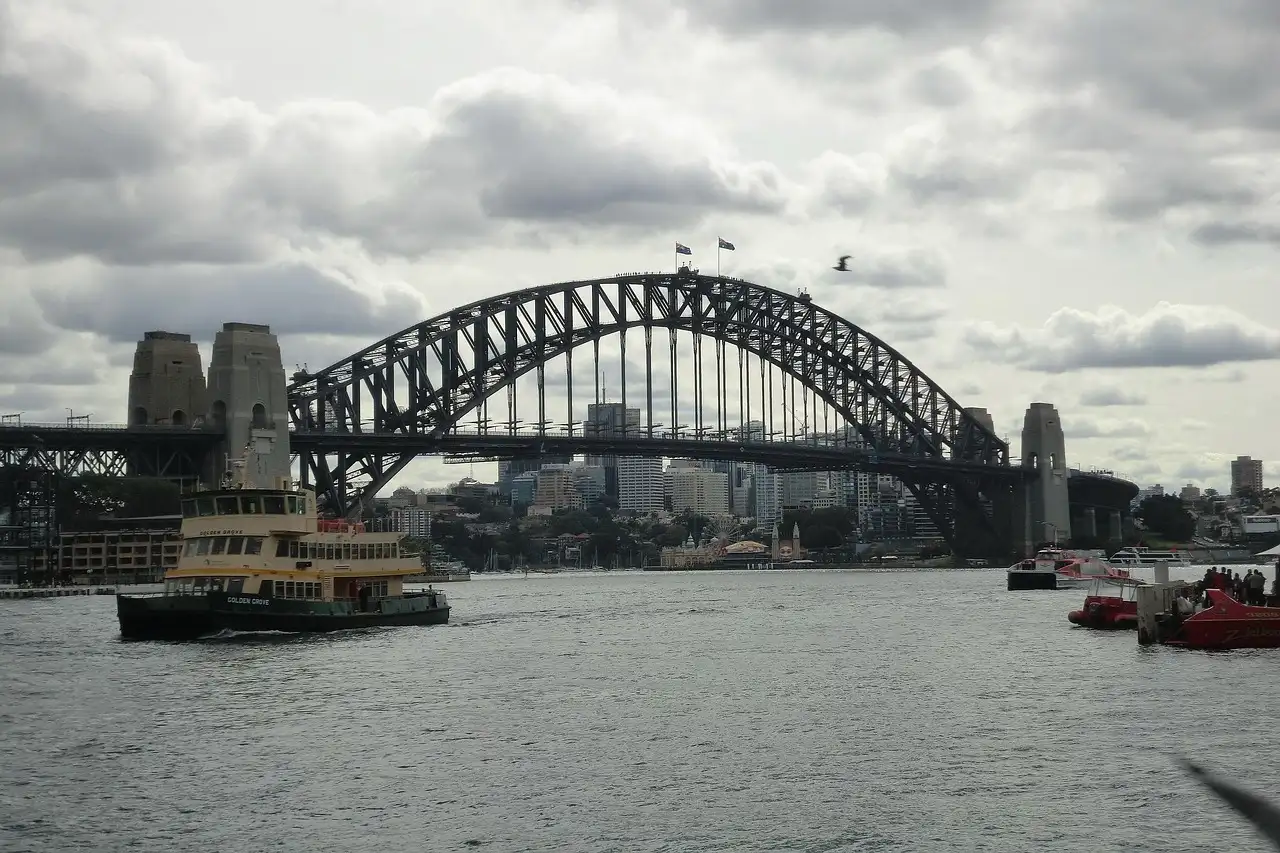The Sydney Harbour Bridge on a cloudy day, with a ferry below