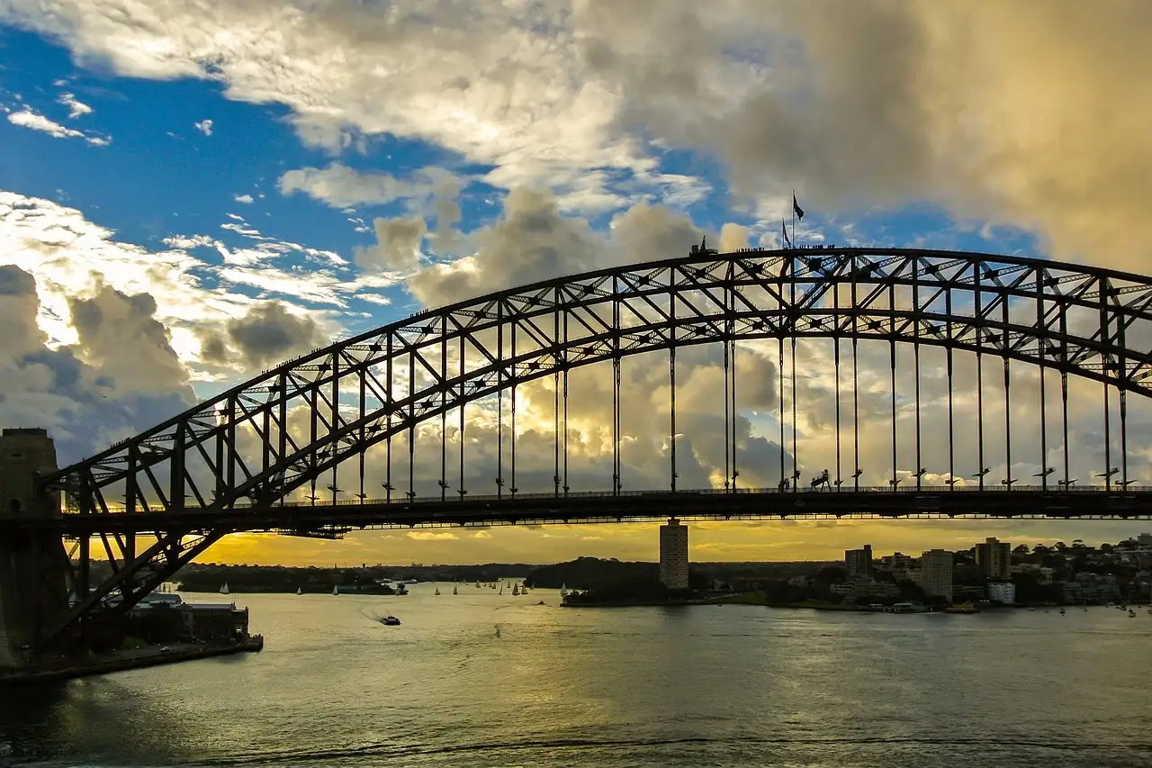 The steel arch of the Sydney Harbour Bridge under dramatic clouds and blue sky