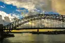 The steel arch of the Sydney Harbour Bridge under dramatic clouds and blue sky
