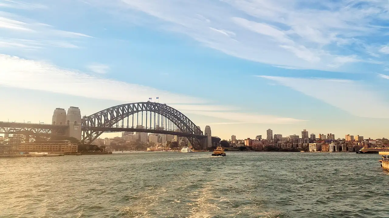 The white wake of a boat on Sydney Harbour, with the Harbour Bridge ahead under a blue sky