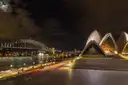 The Sydney Opera House and the Harbour Bridge lit up at night, seen from the Opera House forecourt
