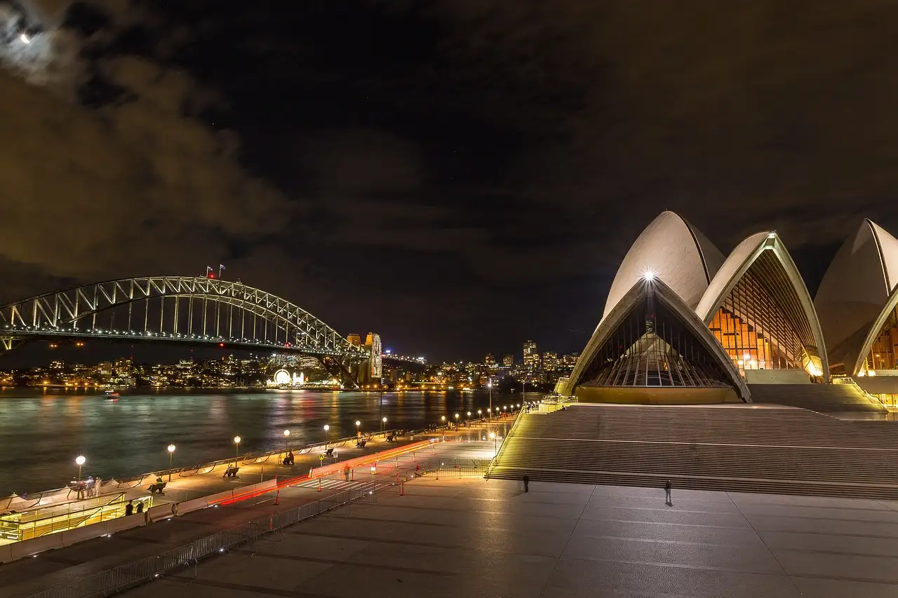The Sydney Opera House and the Harbour Bridge lit up at night, seen from the Opera House forecourt
