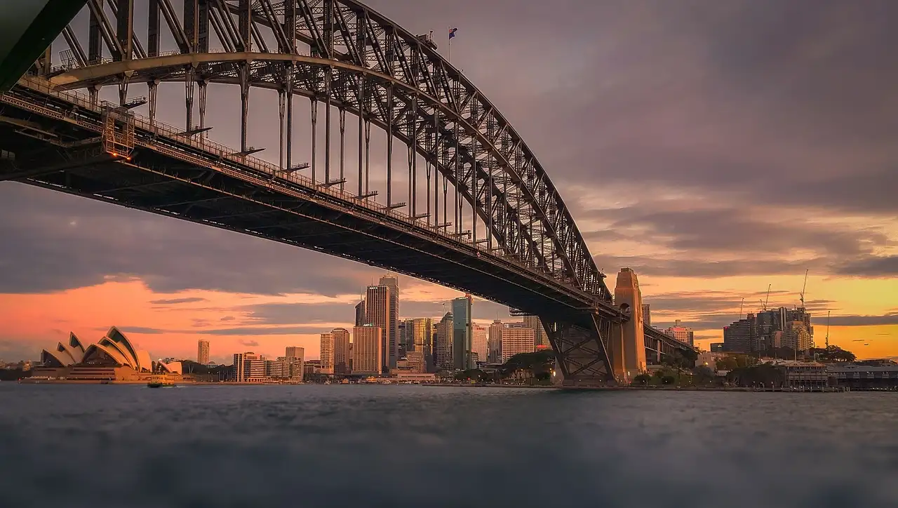 The Sydney Harbour Bridge at sunset, with the Opera House and the city low on the far shore