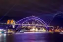 The Sydney Harbour Bridge lit purple during a light festival, with beams of light in the night sky