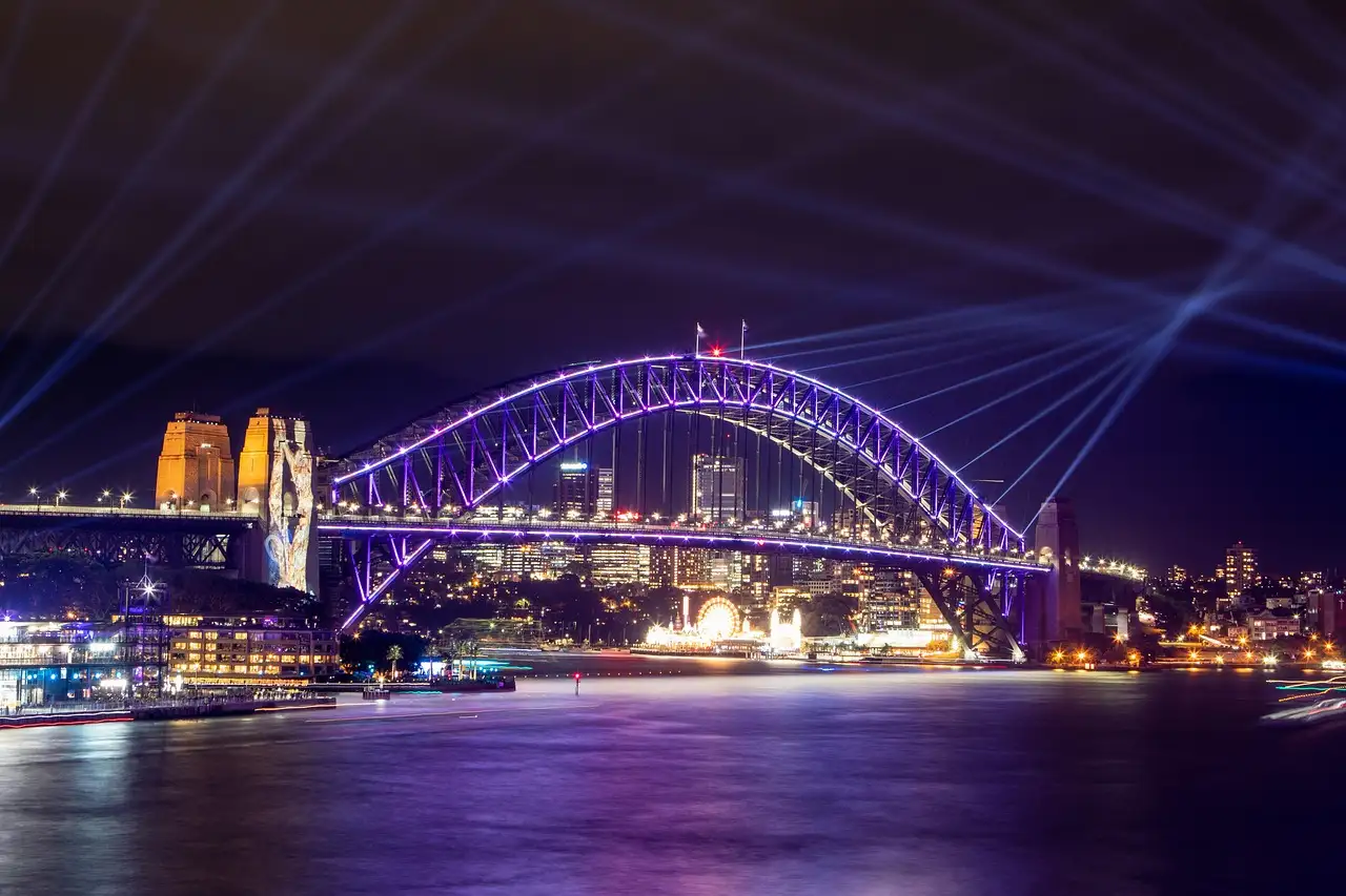 The Sydney Harbour Bridge lit purple during a light festival, with beams of light in the night sky