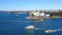 Sightseeing boats crossing blue Sydney Harbour in front of the Opera House on a sunny day