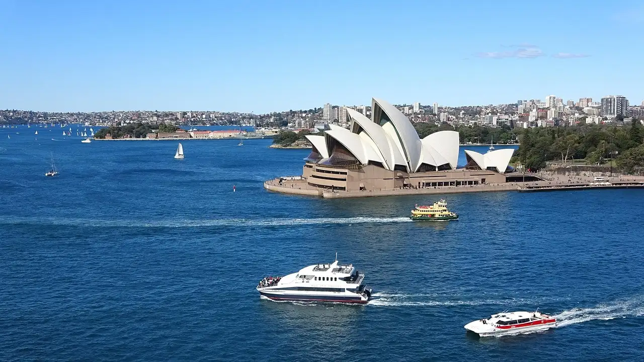 Sightseeing boats crossing blue Sydney Harbour in front of the Opera House on a sunny day