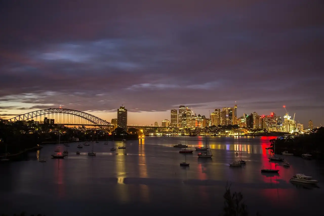 Sydney Harbour at night with boats on the water, the city lights and the Harbour Bridge in the distance