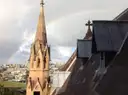 Sandstone spire and roof of St Mary's Cathedral in Sydney with a rainbow over the city