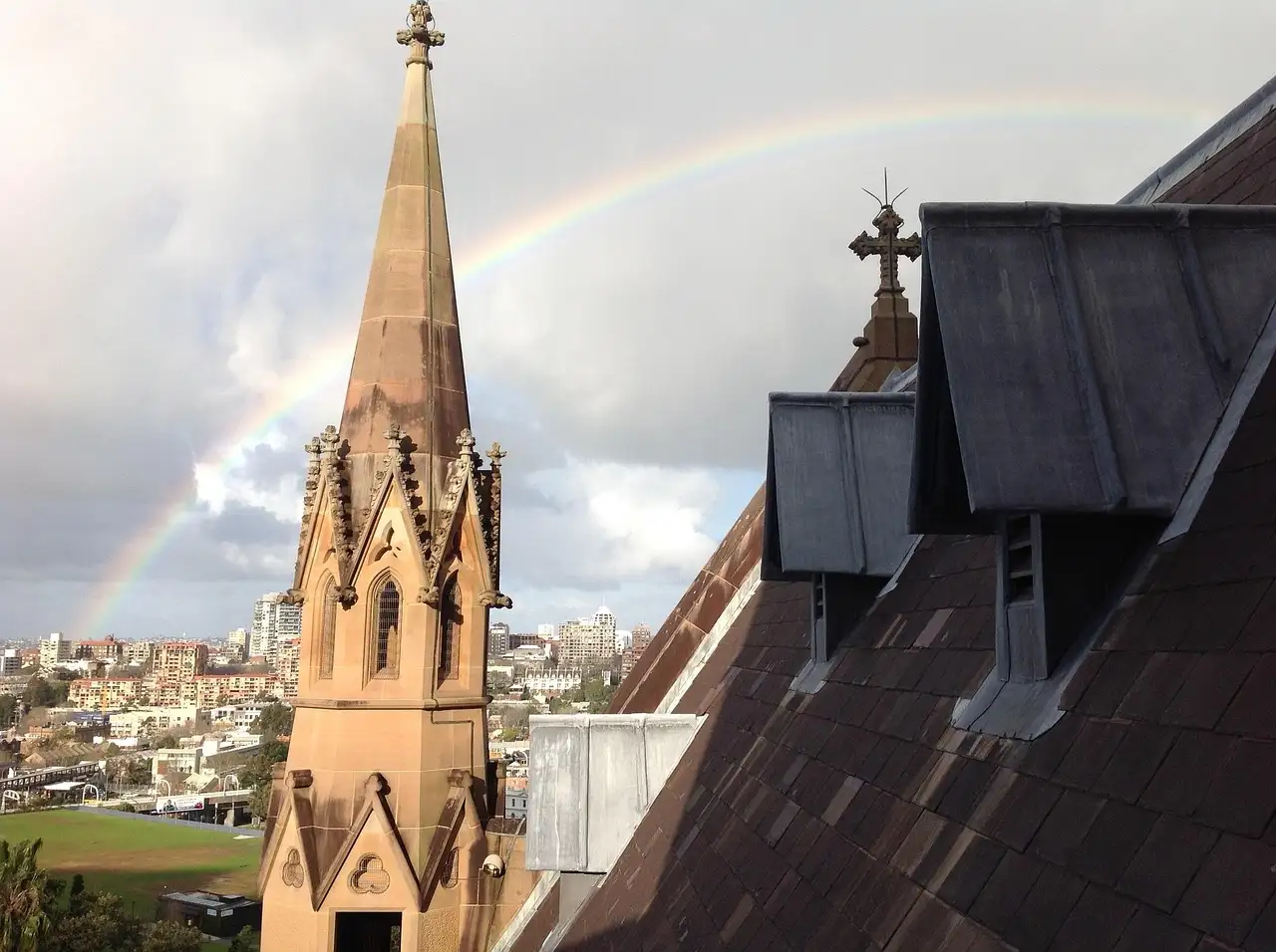 Sandstone spire and roof of St Mary's Cathedral in Sydney with a rainbow over the city