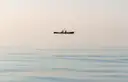 A kayak with two paddlers far out on still water in soft morning light