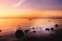 A small kayak on calm water near a rocky shore, with the sun low on the horizon