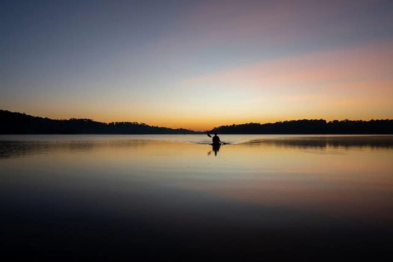 A lone kayaker as a dark shape on still water under a pale sky