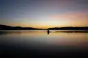 A lone kayaker as a dark shape on still water under a pale sky