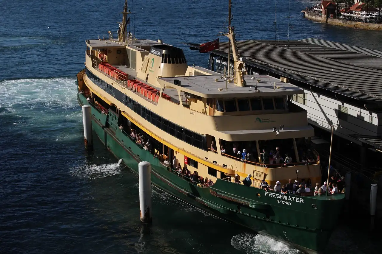 A green-and-cream Sydney harbour ferry with passengers on deck arriving at a wharf