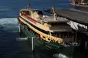 A green-and-cream Sydney harbour ferry with passengers on deck arriving at a wharf