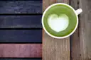 A cup of green matcha latte with a heart in the foam