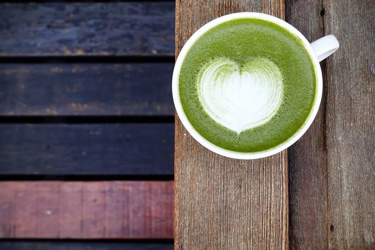 A cup of green matcha latte with a heart in the foam