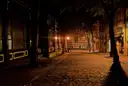 Empty cobbled street at night lit by old lamps, with an old pub at the end