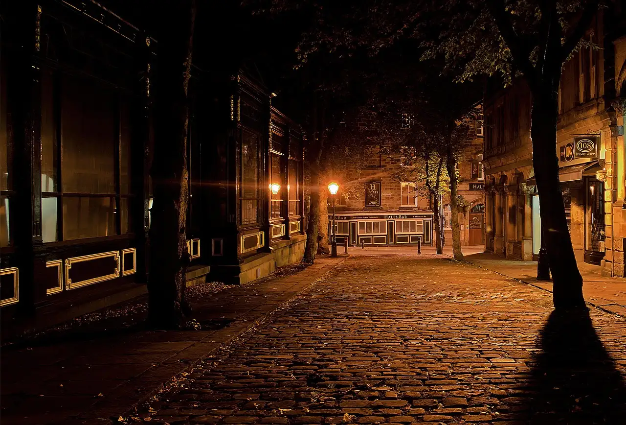 Empty cobbled street at night lit by old lamps, with an old pub at the end