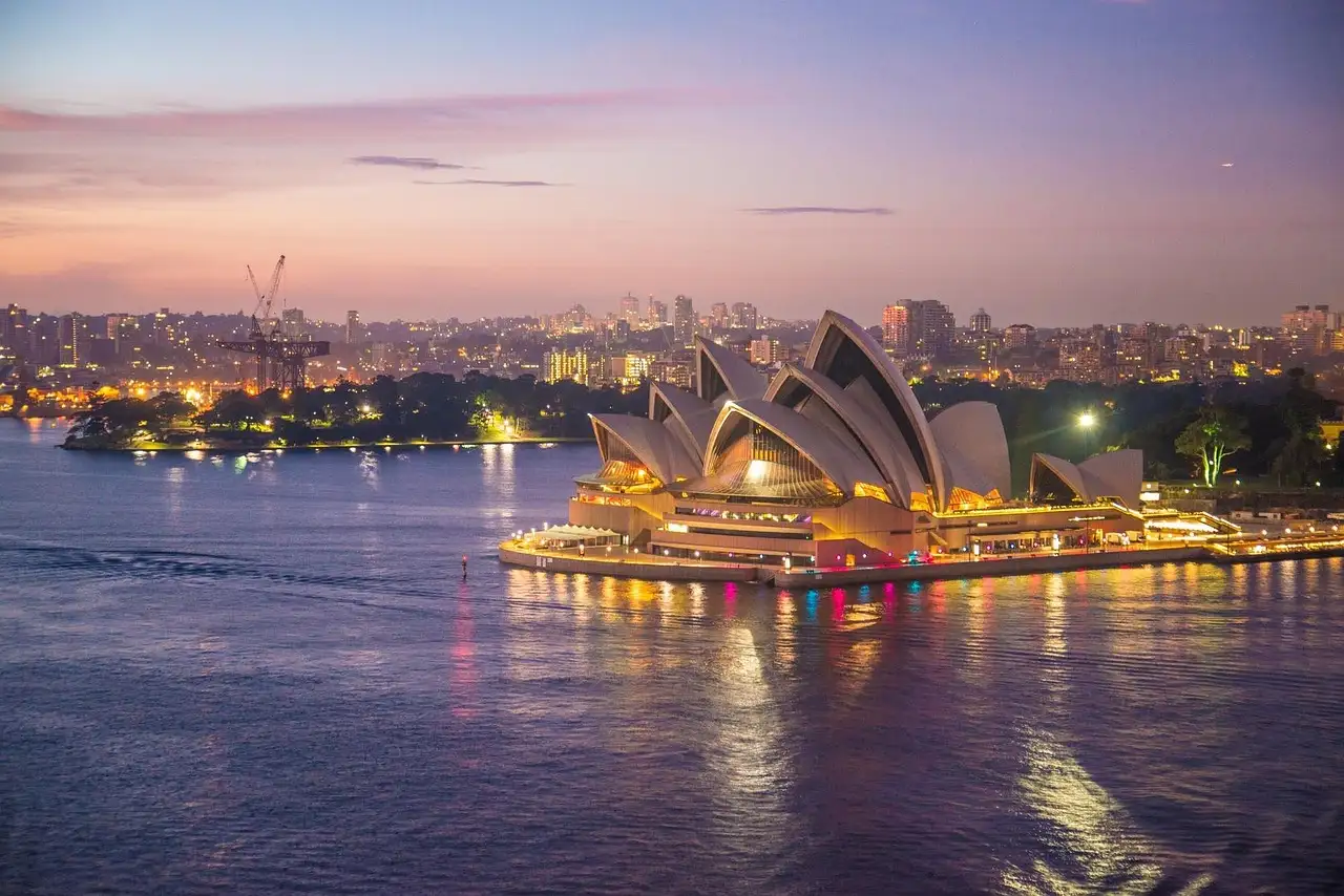 The Sydney Opera House lit up at dusk, seen across the harbour water