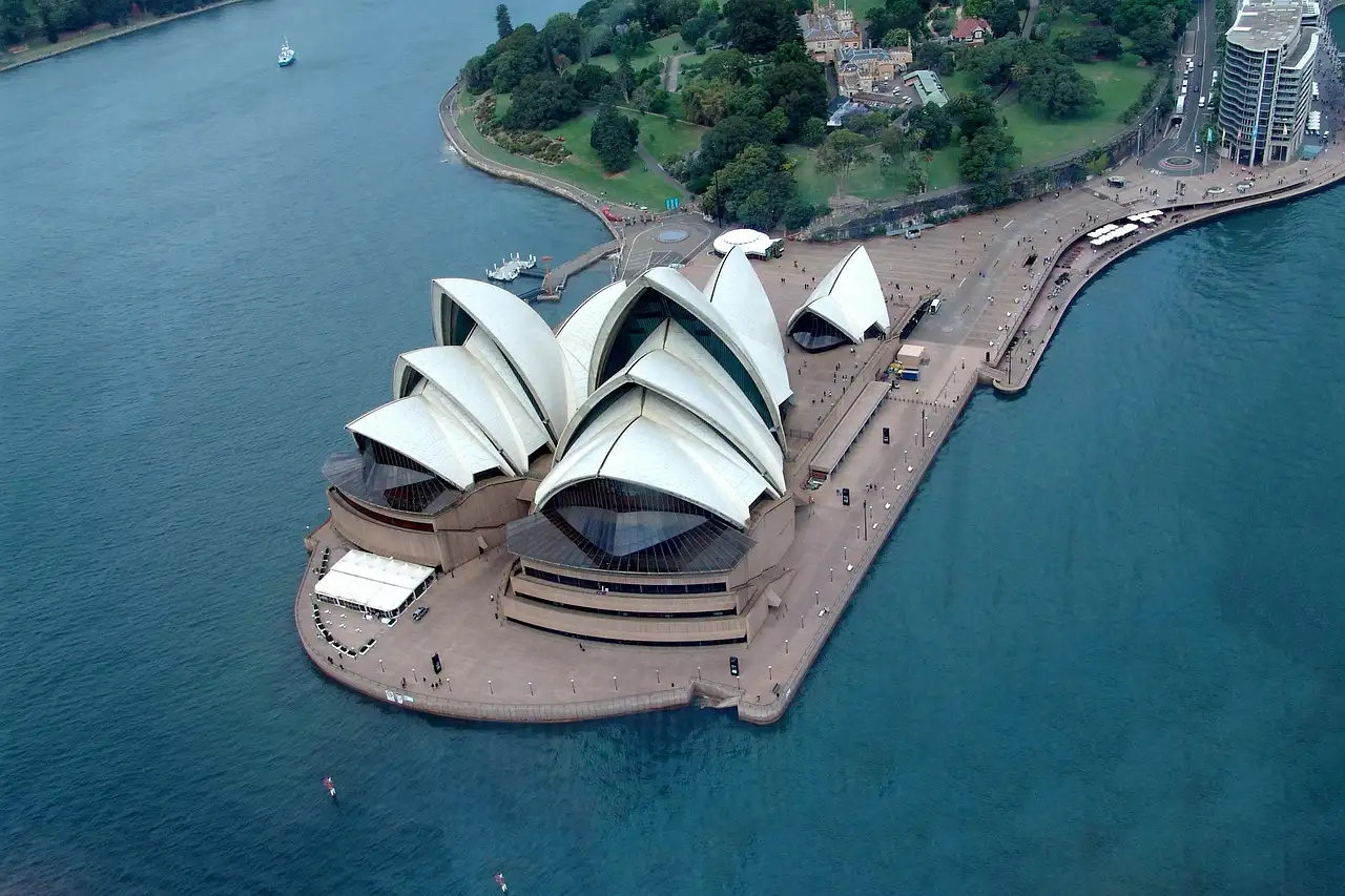 The Sydney Opera House seen from above, its white sails on Bennelong Point surrounded by blue harbour water
