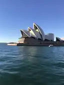 The white sails of the Sydney Opera House seen across the harbour water under a blue sky