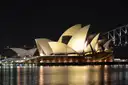 The Sydney Opera House lit up at night, with the Harbour Bridge behind