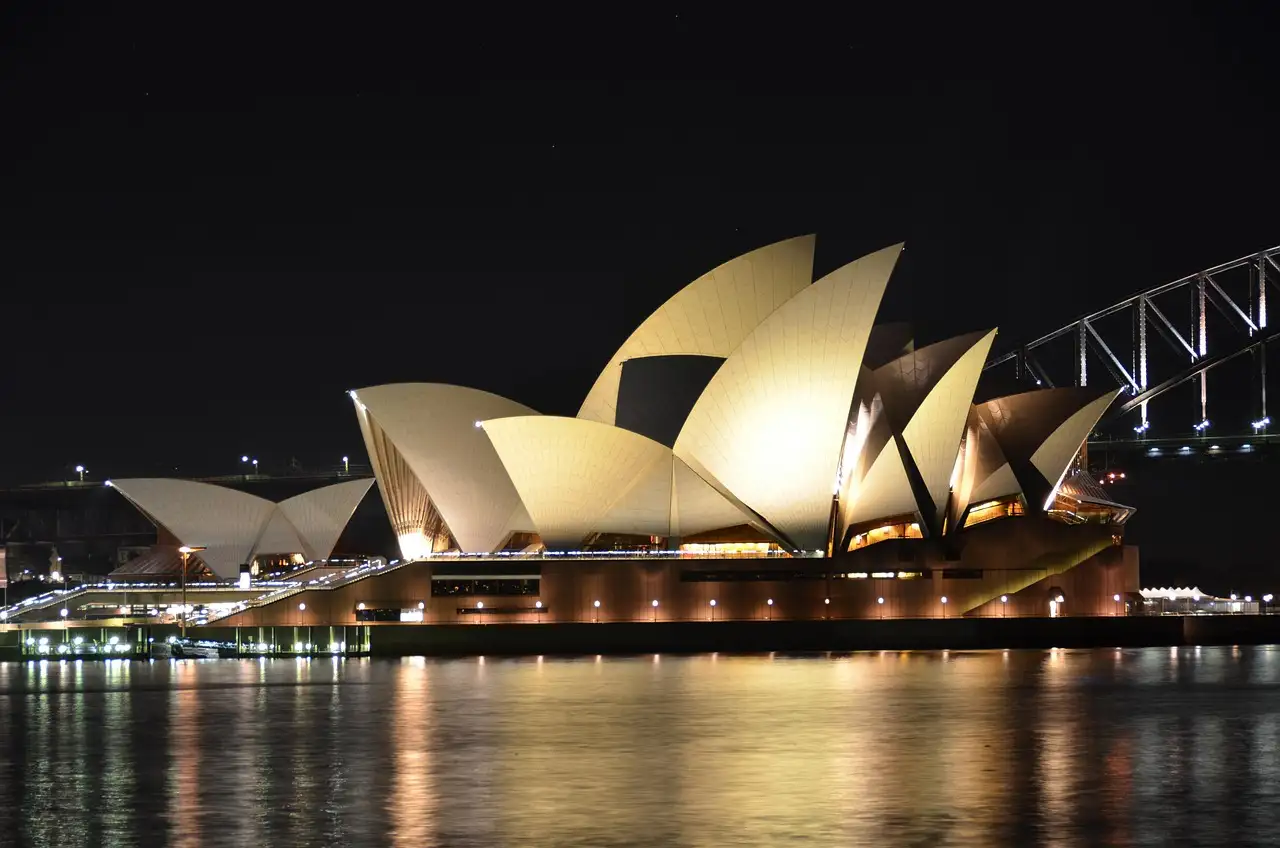 The Sydney Opera House lit up at night, with the Harbour Bridge behind