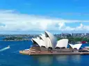 The Sydney Opera House on a sunny day, with a small boat on the blue harbour