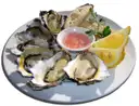 A plate of fresh oysters with lemon wedges and a dipping sauce