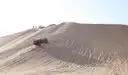 A 4WD vehicle climbing a pale sand dune with tyre tracks in the sand