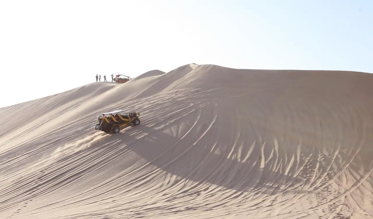 A 4WD vehicle climbing a pale sand dune with tyre tracks in the sand