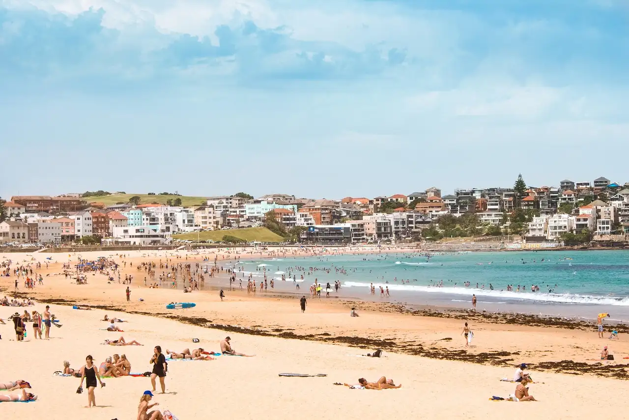 Bondi Beach on a sunny day with swimmers and sunbathers on the sand and houses behind