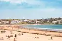 Bondi Beach on a sunny day with swimmers and sunbathers on the sand and houses behind