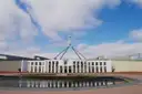 Parliament House in Canberra with its flagpole, under a blue sky with white clouds