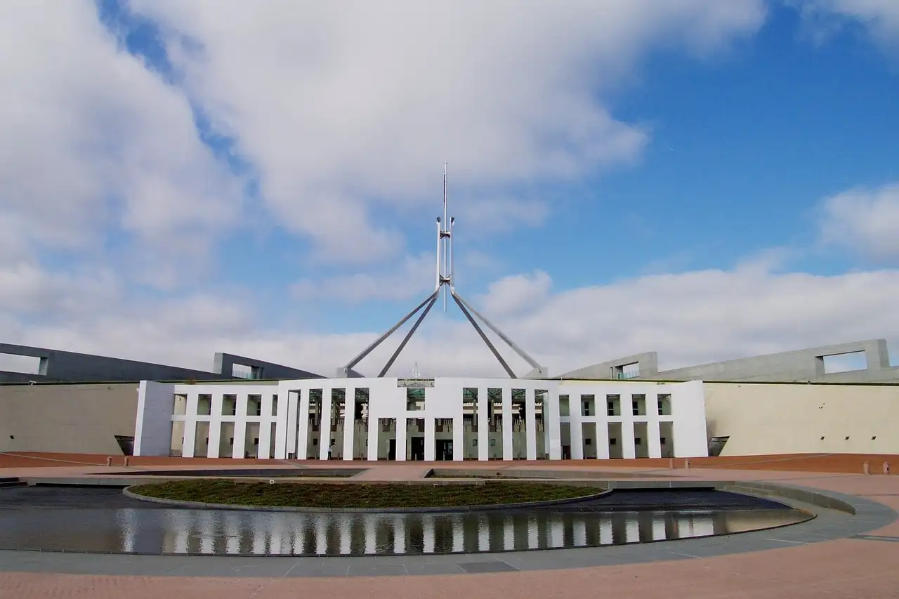 Parliament House in Canberra with its flagpole, under a blue sky with white clouds