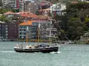 A two-masted sailing ship on Sydney Harbour in front of waterfront houses