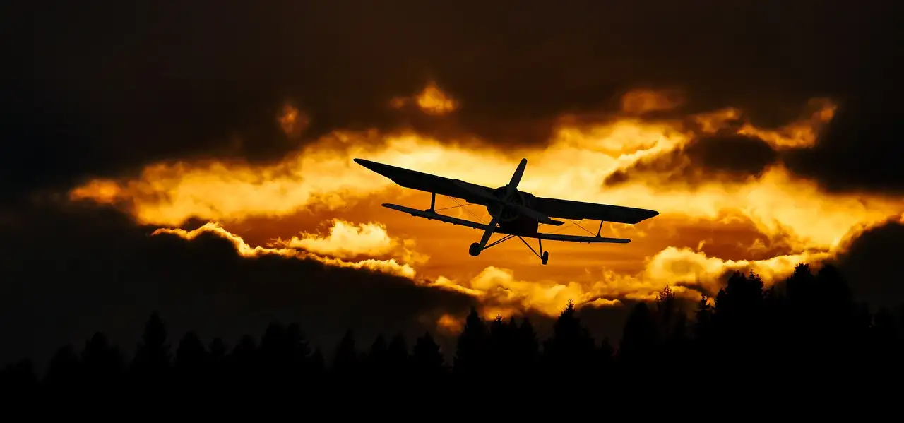 A small plane seen as a dark shape against an orange sunset sky